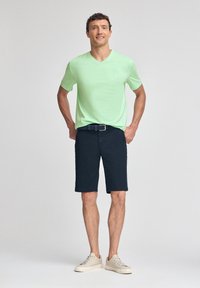 Ljusgrön V-ringad T-shirt, marinblå shorts, beige sneakers. Outfiten har en avslappnad stil med minimal detaljering. Slät textur och passform.