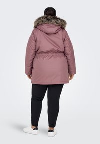 Pink insulated parka with a fur-lined hood, cinched waist, and pockets. Paired with black leggings and white sneakers.