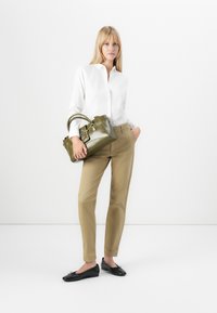 Könnyű, fehér gombos ing, khaki slim-fit nadrág és fekete lapos cipők. Olíva zöld kézi táska lekerekített fogantyúkkal és ezüst kiegészítőkkel.