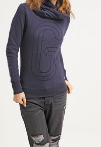 Navy hoodie med cowl-hals, med ett präglat bokstavsdesign "G". Tillverkad av mjukt tyg med ribbade manschetter och en avslappnad passform.