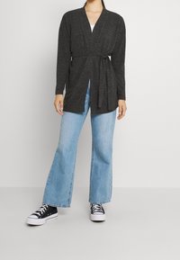 Mörkgrå lång kofta med knytning i midjan, i kombination med ljusblå utsvängda jeans och svarta sneakers. Enkelt, avslappnat design.