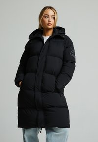 Svart boblejakke med hette, med quiltet design og glidelåslommer. Stoffet virker glatt og isolert for varme.