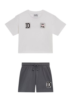 T-shirt bianca a maniche corte e corta con toppe nere e rosse, abbinata a pantaloncini grigio scuro con elastico in vita e toppa nera sulla gamba sinistra.