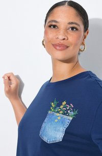 Námořnická modrá tričko vyrobené z bavlny s velkou džínovou kapsou s vyšívanými květinami v žluté, růžové a zelené barvě. Kulatý výstřih, krátké rukávy.