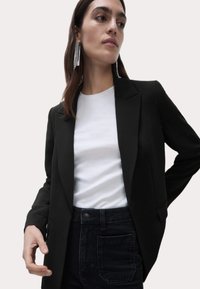 Svart blazer med en strukturerad design, slagkrage och två framfickor, bärs över en vit t-shirt och högmidjade mörka jeans.