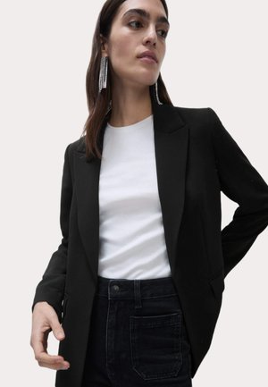 Schwarze Blazer mit strukturiertem Design, Reverskragen und zwei Vorderaschen, getragen über einem weißen T-Shirt und hochgeschnittenen dunklen Jeans.