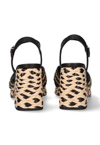 Sandalias de tacón trenzadas en negro y beige, con un tacón grueso trenzado y una correa negra en el tobillo con un detalle de hebilla dorada.