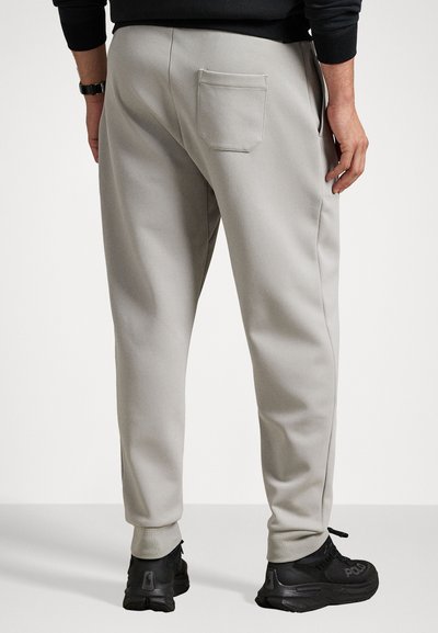 Ανοιχτό γκρι φόρμες από μαλακό υλικό, με κομμένες πόδια, ριμπ μανσέτες και πίσω τσέπη. Συνδυασμένες με μαύρα αθλητικά παπούτσια.