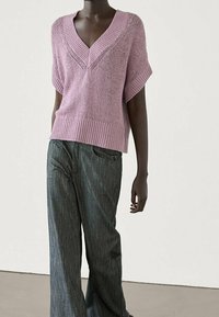 Vaaleanpunainen neulepusero, jossa on leveä V-kaula-aukko ja lyhyet hihat, yhdistettynä tummanharmaisiin leveälahkeisiin farkkuihin, esittelee rentoa ja mukavaa istuvuutta.