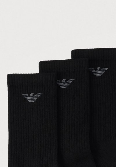 Svarte bomullsstrømper med ribbet struktur og en grå ørnlogo nær kanten. Tre par vist vertikalt med en teksturert overflate.