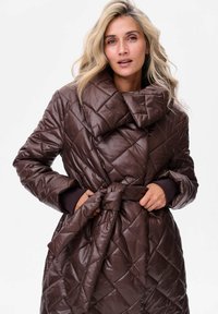 Brązowa pikowana kurtka puchowa z dużym kołnierzem, posiadająca pasek w talii oraz ściągacze na rękawach. Błyszcząca, gładka tekstura zewnętrzna.