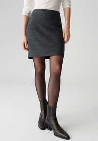 Minigonna di lana grigia con una leggera forma a trapezio, abbinata a calze nere trasparenti e stivaletti alla caviglia con punta quadrata e tacco spesso.