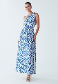 Maksi haljina s jednim ramenom u bijeloj boji s plavim zebrinim prugama, s vezanjem u struku, drapiranim dizajnom i glatkom teksturom tkanine.