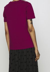 Tajt kortärmad t-shirt i djup magenta, gjord av mjuk bomull, med en klassisk rundhals och en slät yta.