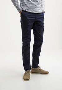 Námořnické kalhoty ve slim fit, vyrobené z hladké látky. V kombinaci s světle hnědými semišovými botami a texturovaným šedým svetrem.