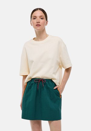 T-shirt oversize crème associé à une jupe élastique turquoise avec des accents orange et un cordon tressé. Texture lisse, style décontracté.