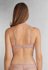 Lichtroze bh met kant achteraan, verstelbare bandjes, kantaccenten en een haak-en-oogsluiting. Glad materiaal met een delicate afwerking.