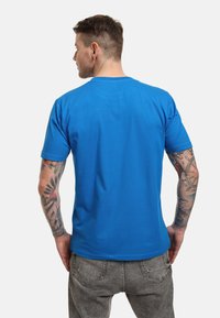 Camiseta de manga corta azul, hecha de una mezcla de algodón, con cuello redondo y una textura suave. Sin logotipos ni patrones visibles.