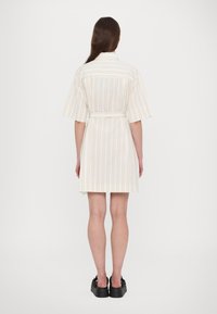 Abito a maniche corte a righe con vita rialzata, caratterizzato da linee verticali beige e pastello, realizzato in un tessuto leggero. Scarpe con zeppa nera.