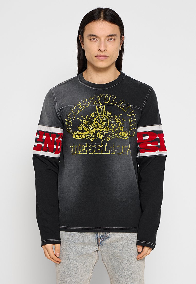 Schwarzes Langarm-T-Shirt mit grau ausgewaschenen Bereichen. Mit gelber grafischer Schrift und roten Akzenten an den Ärmeln. Baumwollmaterial, lockere Passform.