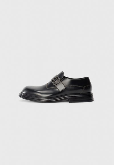 Black leather dress shoe with a large buckle strap closure, detailed stitching, and a layered sole, photographed on a white background.