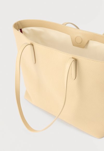 Μπεζ δερμάτινη τσάντα ώμου με ομαλή υφή, δύο μακριές λαβές και ανοιχτό άνω μέρος που αποκαλύπτει ελαφρύ εσωτερικό χρώμα.