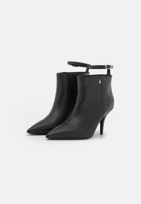 Botas de cuero negras hasta el tobillo con punteras puntiagudas, tacones delgados y correas ajustables en el tobillo con un acento plateado en el lateral.