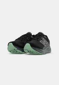 Melnas un piparmētru zaļas New Balance skriešanas kurpes ar mīkstiem zoliņām un "N" logotipiem, izliktas uz balta fona.
