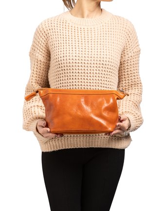 Borsa cosmetica in pelle di un vivace arancione, caratterizzata da una texture liscia e una chiusura con zip. Tenuta da una persona che indossa un maglione beige lavorato a maglia.