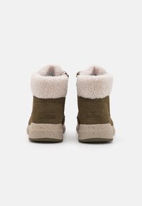 Une paire de bottines vert olive avec des semelles beige mouchetées et une doublure en fausse fourrure blanche visible en haut, vue de l'arrière.