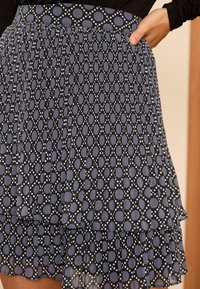 Gonna nera con strati a volant, caratterizzata da motivi ovali e a pois alternati in viola e bianco, e una vita patternizzata.