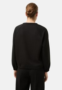 Černá mikina s raglánovými rukávy, elastickými manžetami a volným střihem. Hladká textura, jednoduchý design a jednobarevná bez vzorů či akcentů.