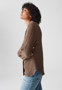 Brauner, strukturierter Strickcardigan mit lockerer Passform, langen Ärmeln und abgerundetem Saum, kombiniert mit hellblauen Jeans.