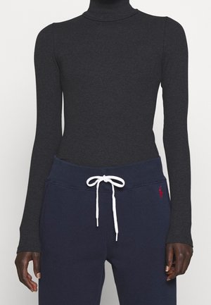 Slim fit mørkegrå rullekrave trøje kombineret med marineblå joggingbukser med hvid snor og lille rødt logo på hoften.