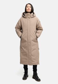 Lang beige parka med hætte, der har frontlynlås, to sidelommer og en afslappet pasform. Parret med sorte kampstøvler.