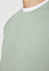 Ljust grön bomullströja med rund halsringning och korta ärmar, med en kontrasterande vit innermudd och en mjuk textur.