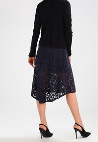 Tmavě modrá krajková sukně s asymetrickým lemem, překrytá jednobarevným tmavě modrým podšívkou. Černý top s dlouhým rukávem a černé boty na vysokém podpatku doplňují vzhled.