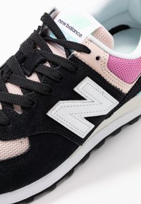 Baskets en suède noir et mesh avec un logo "N" blanc, des accents roses et une surface texturée. Elles sont dotées de lacets noirs et d'une semelle blanche.