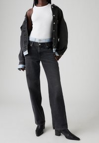 Svart jeansjacka, vit linne och svarta jeans med vida ben. Märkbara detaljer inkluderar ljusblå accenter på jackans ärmslut och en hög midja.