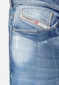 Uvolněné světle modré džíny z denimu s distressed texturou. Obsahují malou značkovou etiketu v zadní kapse. Zdobení zahrnuje třepené okraje.
