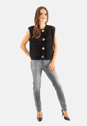 Gilet en maille noire avec de grands boutons argentés, doté de deux poches avant. Associé à un jean gris clair et des talons pointus noirs.