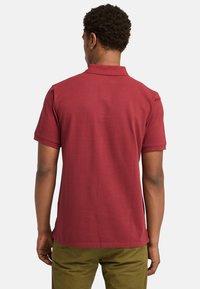Körsbärsröd polo t-shirt med klassisk krage, korta ärmar och en jämn, enfärgad textur. Baksidan är enkel utan ytterligare mönster eller detaljer.