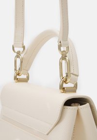 Kremowa skórzana torebka o teksturowanym wykończeniu. Posiada złote okucia i wyrafinowany kształt. Szczegółowe uchwyty z ogniwami łańcucha.