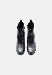 Černé kotníkové boty s lesklým lakovaným povrchem, kulatou špičkou, šněrovacím designem a výškou ke kotníkům. Na zadní straně mají poutko pro snadné obouvání.
