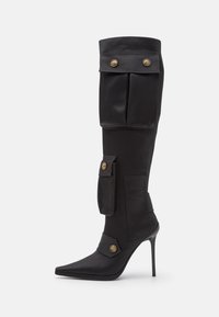 Bottes noires montantes jusqu'à la cuisse en cuir lisse, avec deux grandes poches, des boutons-pression dorés et un bout pointu sur un talon stiletto haut.