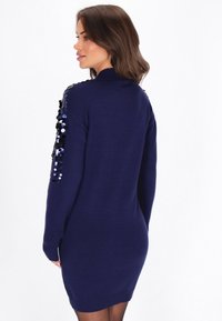 Abito a maglia blu navy con maniche lunghe decorate con paillettes sulle spalle, polsini e orlo a coste, e una silhouette aderente.