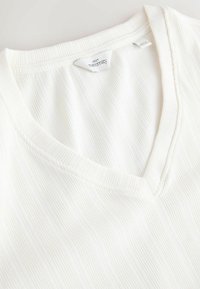 Biały, ciążowy top z dekoltem w serek, z prążkowaną fakturą i subtelnymi pionowymi liniami, z metką z nazwą marki.