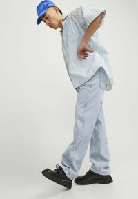  Lichtblauw gestreept shirt met korte mouwen, lichte denim jeans en zwarte veterschoenen. Het shirt heeft een relaxed fit en de jeans zijn wijder met zichtbare naden.