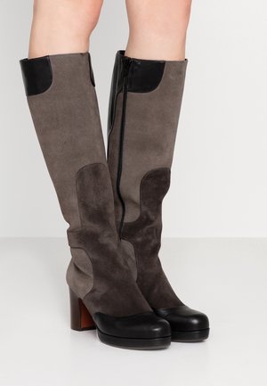 Damskie kozaki do kolan z szarą welurową cholewką, czarnymi skórzanymi nakładkami na palce i kołnierzami na piętach, obcasami typu blok oraz zamkami błyskawicznymi po bokach na białym tle.