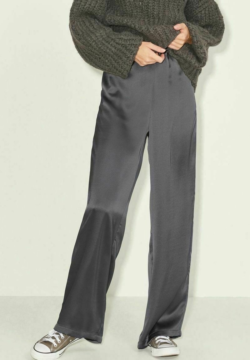 Gray satin wide-leg pants with a smooth texture, featuring an elastic waistband and paired with brown sneakers. Knitted olive sweater above.